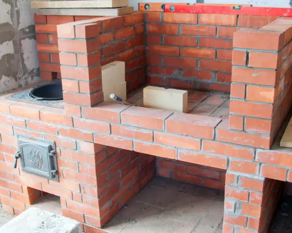 Construcción de chimeneas de obra de leña. Ladrillos rojos y mortero gris forman una estructura robusta, lista para encender el fuego.
