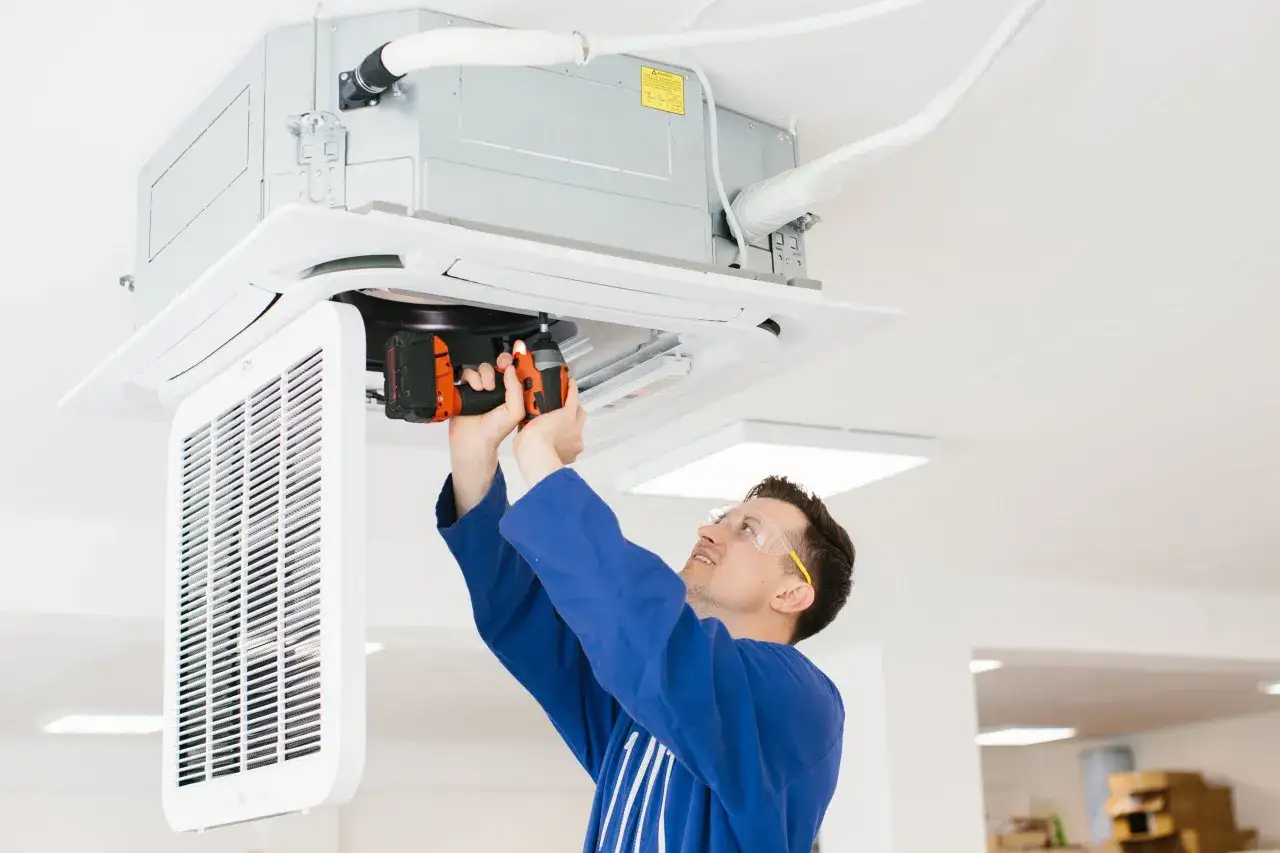 Técnico realiza instalación de aire acondicionado en el techo, usando un taladro.
