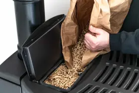 Persona rellena un compartimento de estufa de pellets. Considera el instalar estufa pellets precio para un hogar eficiente.